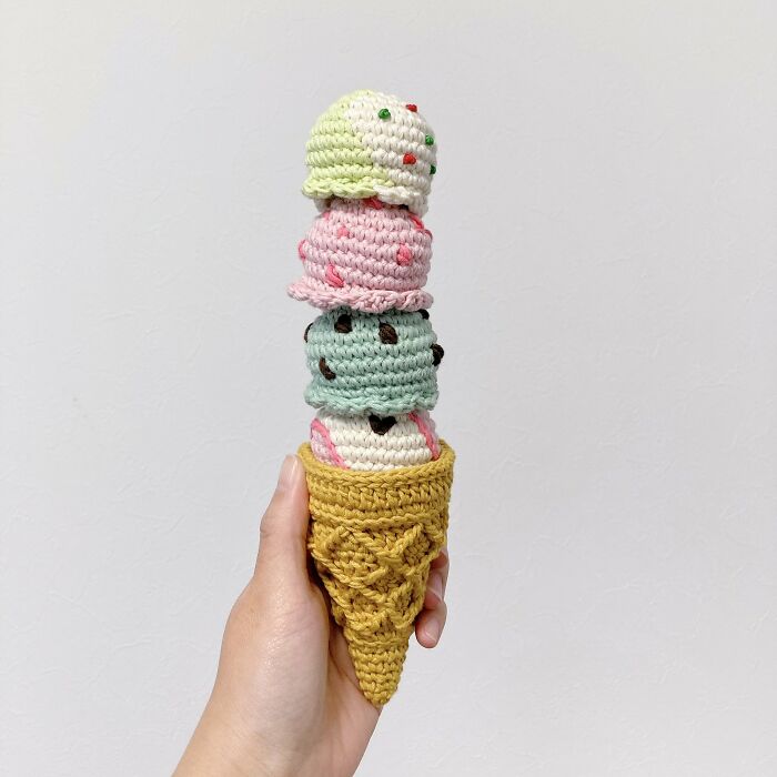 Hand holding a crocheted realistic food-inspired ice cream cone with multiple colorful scoops by Japanese fiber artist.