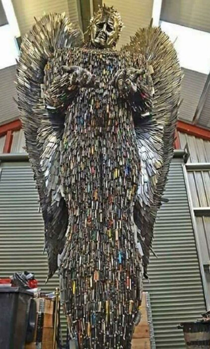 Sculpture of an angel made entirely from numerous knives, displayed indoors with industrial surroundings.