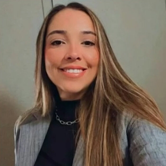 Smiling woman with long hair wearing a gray blazer and black top, related to plastic surgeon arrested after butt lift procedure.