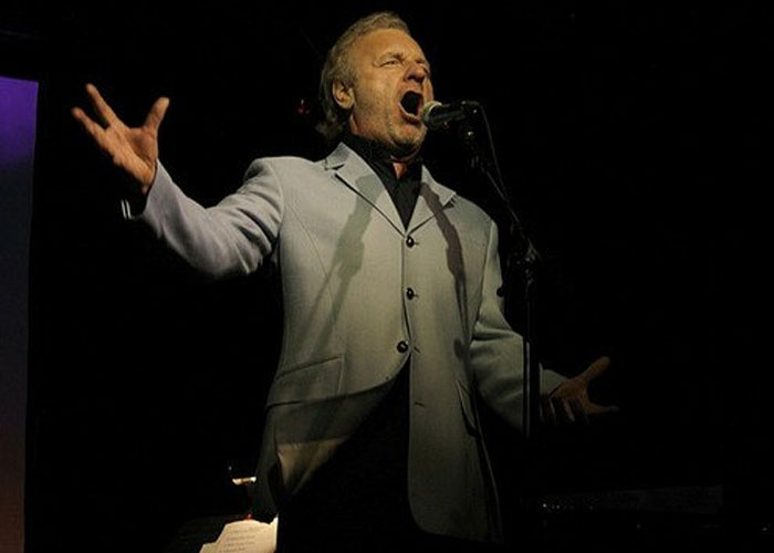Man passionately singing on stage with microphone in a dramatic pose illustrating incredible coincidences concept.
