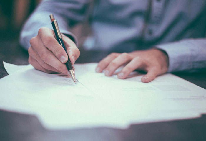 Person holding a pen and writing on documents, illustrating brilliant loopholes exploited to save money.