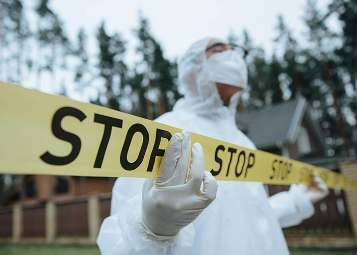 Person in protective suit holding stop tape at an outdoor scene for terrifying true stories investigation.