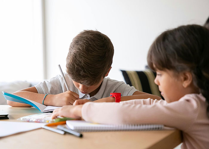 Two children focused on writing and studying at a table, highlighting the impact of historical events on society.