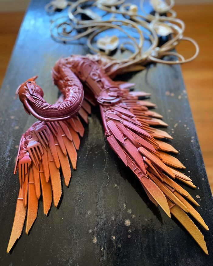 Intricate animal sculpture made from recycled trash, featuring a colorful bird with mechanical wings and curling metal vines.