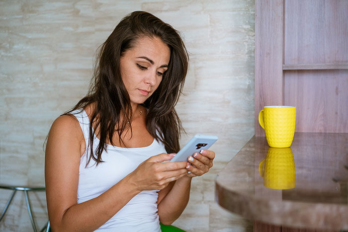 Woman looking suspicious while using phone, reflecting concerns about nannying and husband&rsquo;s coworker situation.