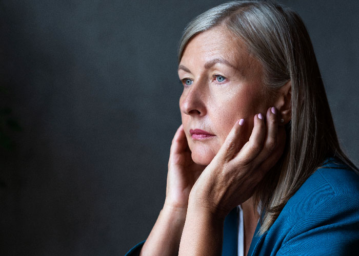 Woman with gray hair in a blue jacket looking pensive, reflecting on feelings related to mother poisoned me experience.