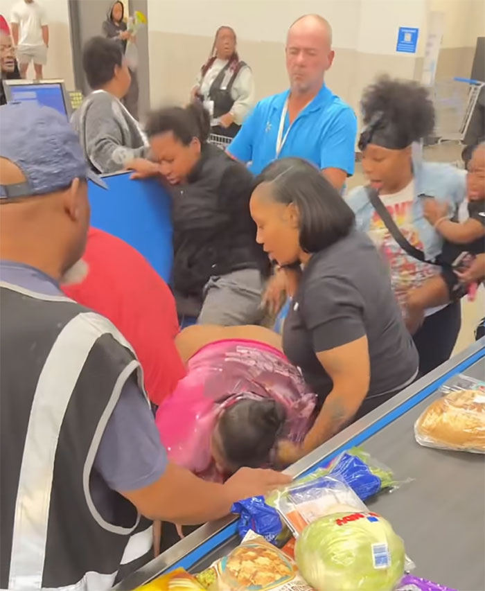 Angry mob surrounding and confronting Walmart employee near checkout with groceries visible on the counter in chaotic scene