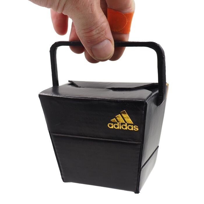 Hand holding a black Adidas box-shaped bag made from waste materials as witty commentary on modern life.
