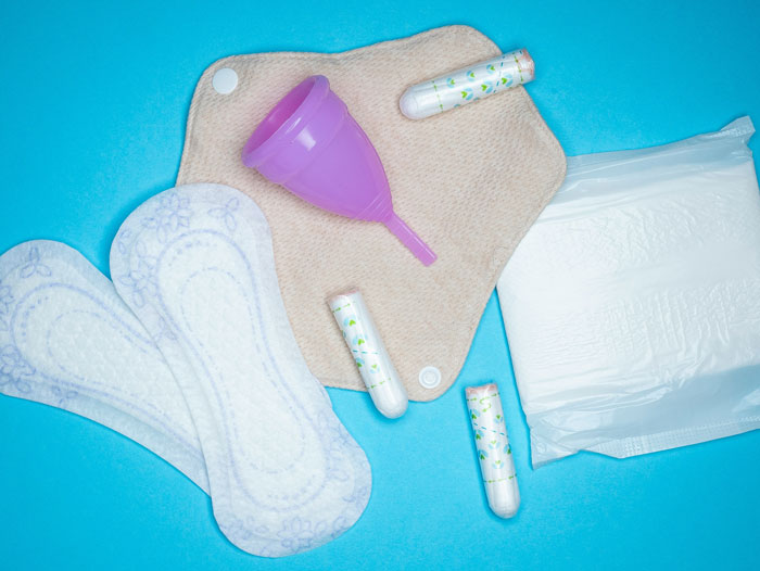 Menstrual hygiene products including pads, tampons, and a menstrual cup on a blue background representing the girl&rsquo;s health context.