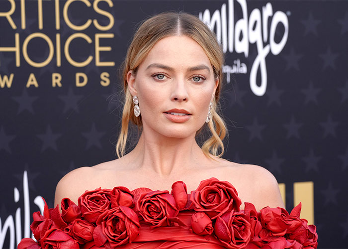 Margot Robbie at Critics Choice Awards in a red rose dress, related to Wuthering Heights teaser and 1800s theme.