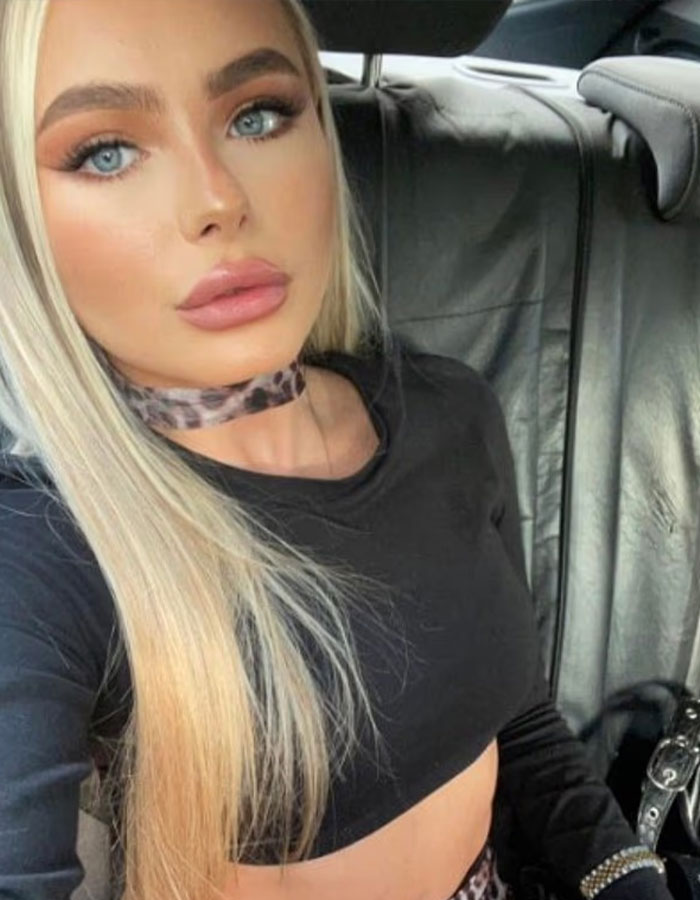 Young glamorous law student with long blonde hair and blue eyes wearing a black crop top inside a car.