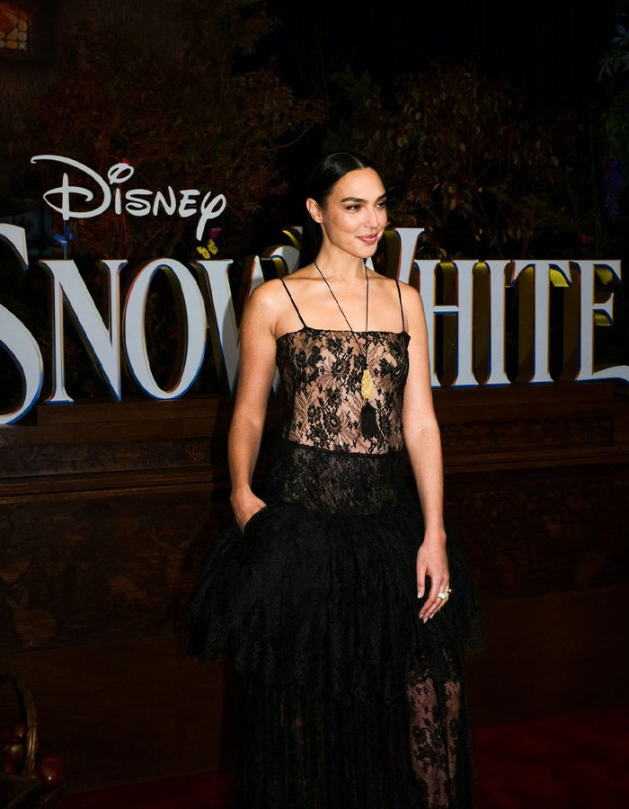 Gal Gadot in a black lace dress posing at a Disney Snow White event, highlighting her absence from Venice Film Festival.