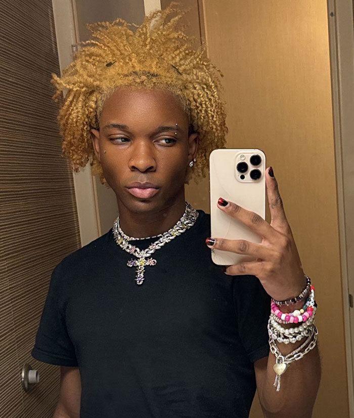 Singer takes selfie in mirror wearing black shirt and layered jewelry after decomposing body was found in abandoned Tesla case