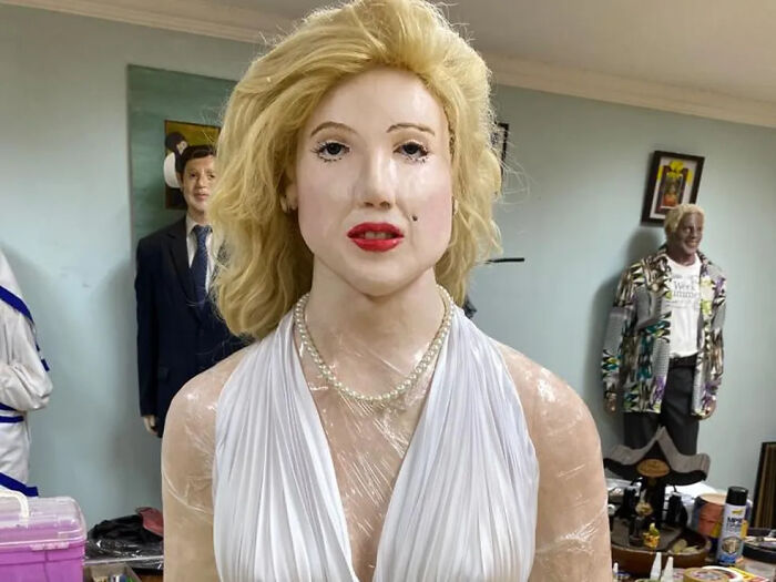 Wax sculpture of a famous figure with blonde hair and white dress, showcasing creepy and hilarious artistic craftsmanship.