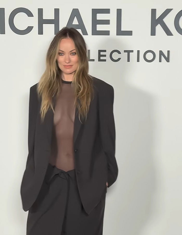 Olivia Wilde in a sheer outfit showing toned abs, wearing an oversized black blazer at New York Fashion Week event.
