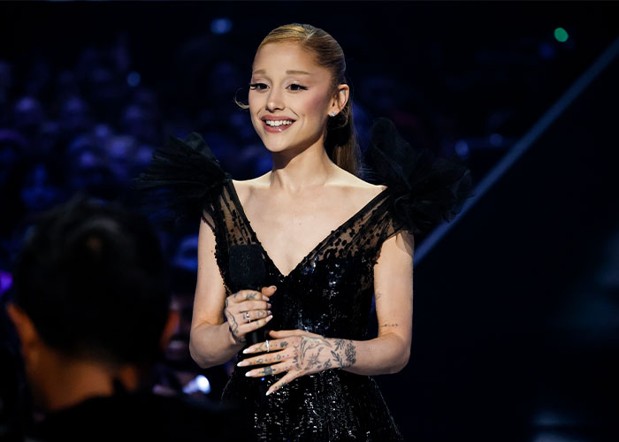 Ariana Grande smiling on stage wearing a black dress while Ethan Slater addresses breakup rumors. Ariana Grande smiling on stage wearing a black dress while Ethan Slater addresses breakup rumors.