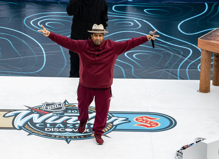 Performer in a maroon outfit and hat on stage during a loud concert fans wish they’d skipped due to clear hatred.