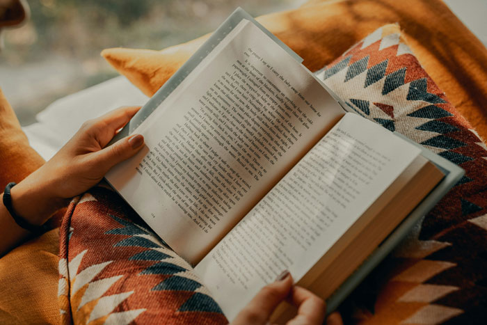 Person reading a book on a patterned blanket, evoking the eerie feeling of creepy things while home alone.