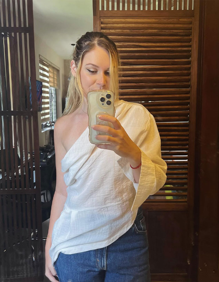 Young woman in casual white top and jeans taking a mirror selfie, related to poisoned limoncello news event.