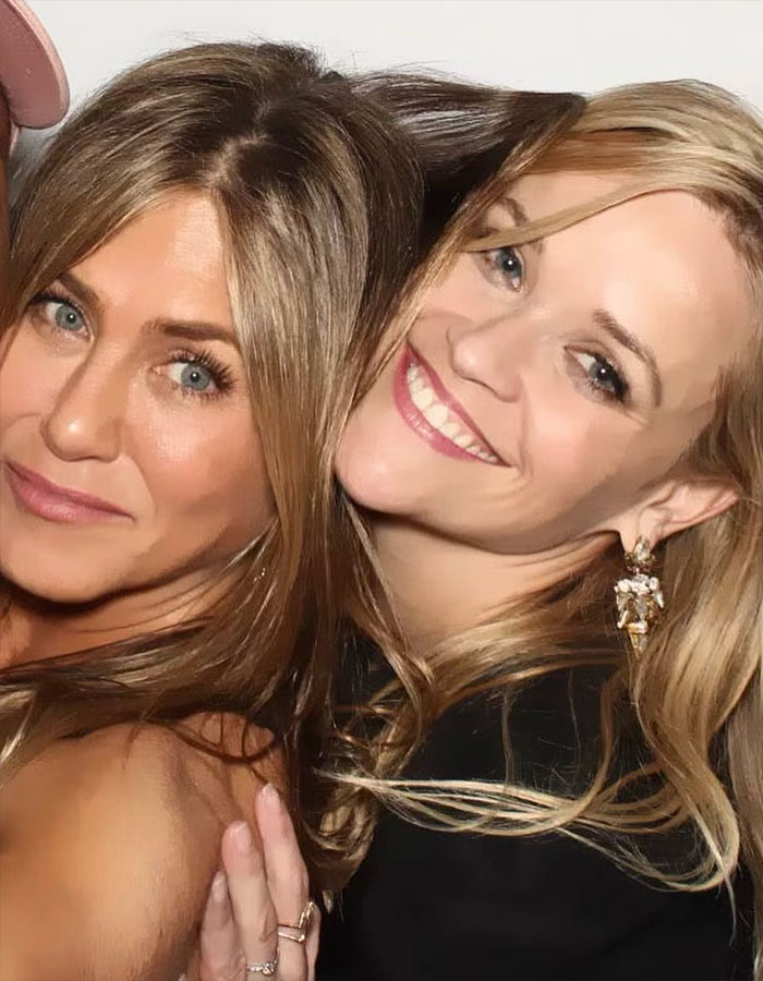 Jennifer Aniston and Reese Witherspoon smiling closely together in a candid, friendly moment.