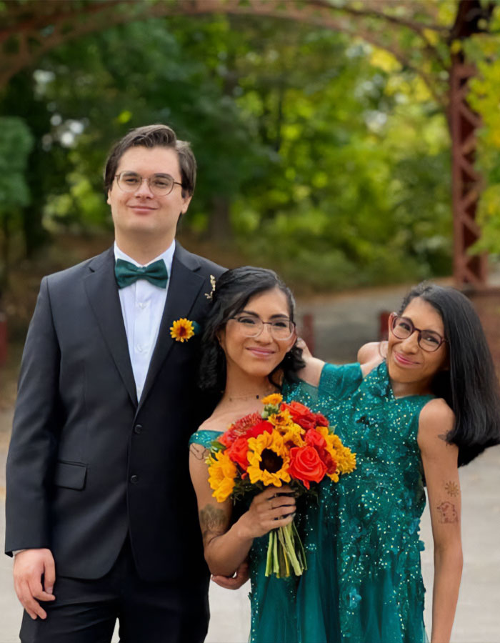 Conjoined twin Carmen Andrade in a green dress with husband and family, smiling outdoors with autumn foliage background.