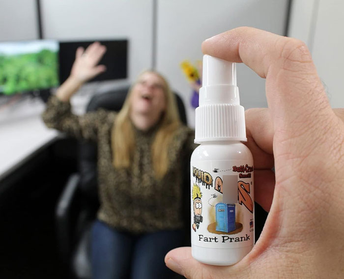 Hand holding a prank fart spray bottle with a blurred woman reacting in a school office, related to teacher using poop spray incident.