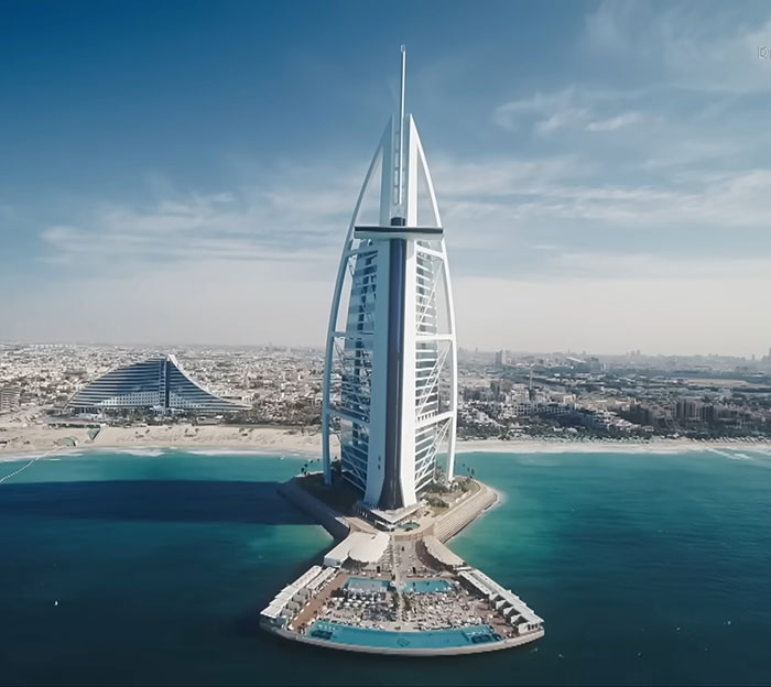 Aerial view of Dubai coastline with iconic Burj Al Arab and cityscape under a partly cloudy sky.