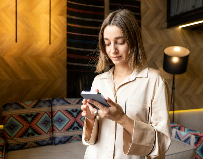Mujer usando teléfono móvil en sala moderna, ejemplificando cómo los teléfonos ayudan a descubrir verdades ocultas.