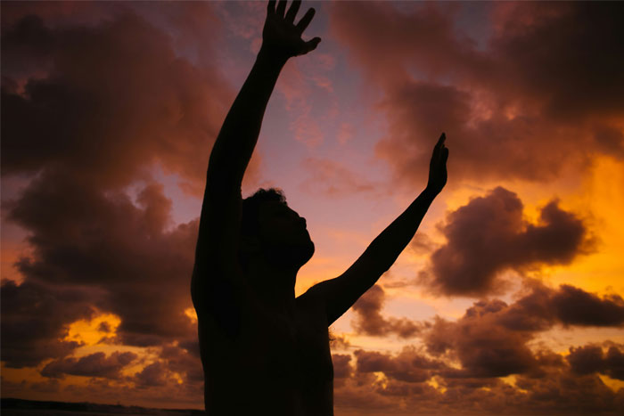 Silhouette of a man raising hands against a dramatic sunset sky symbolizing RaptureTok and end of the world prediction.