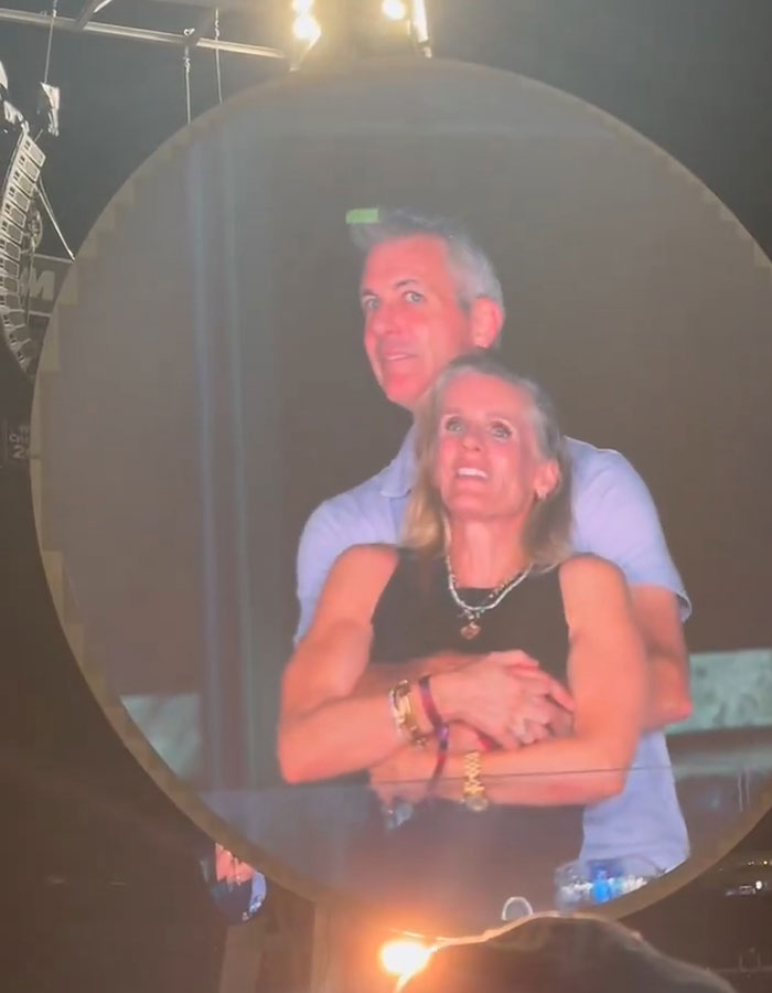 Couple embracing in front of stage lights during Coldplay concert amid Kristin Cabot scandal rumors.
