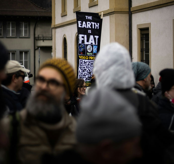 Protesters in a crowd holding a sign promoting flat earth theory, illustrating common sense collapse in groups.