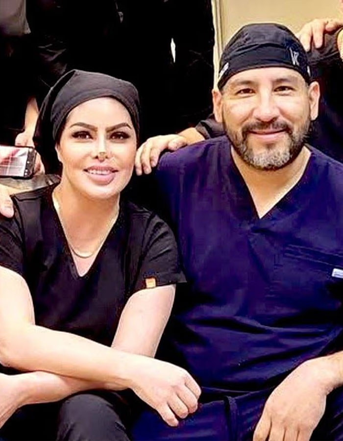 Surgeon who performed fatal breast enlargement on 14-year-old, seated next to a woman in black scrubs, both smiling.