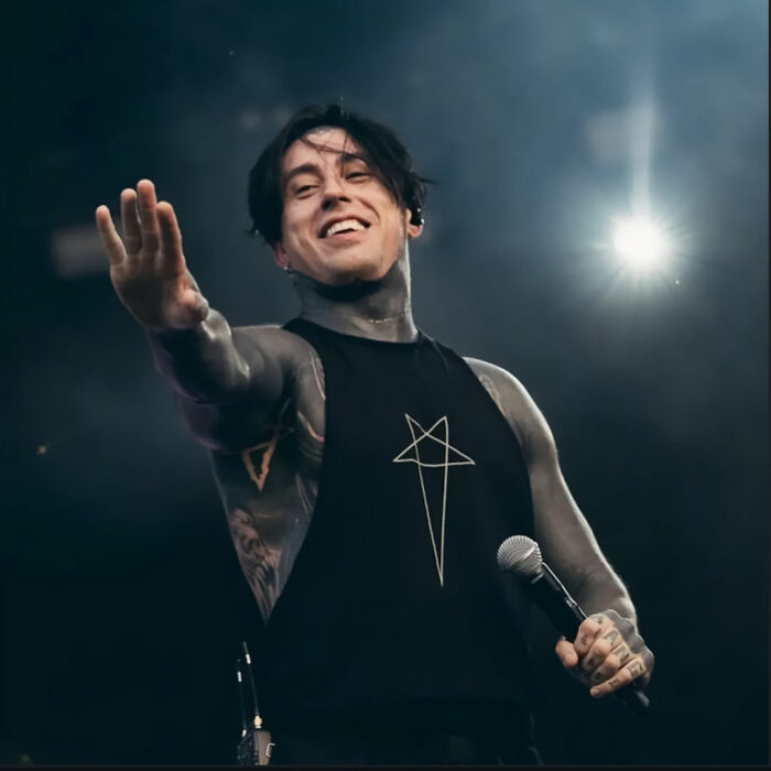 Ex-con rock star performing on stage, smiling and reaching out while holding a microphone during a concert.