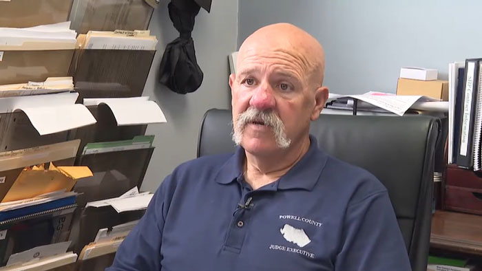 Man with mustache in Powell County shirt sitting in office chair, surrounded by files, discussing paramedics saving snakebite victim. Man with mustache in Powell County shirt sitting in office chair, surrounded by files, discussing paramedics saving snakebite victim.