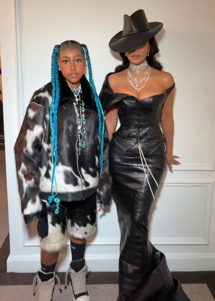 Woman in black leather dress and hat with daughter in cow print outfit and blue braids posing indoors representing Kanye West pain and betrayal list.