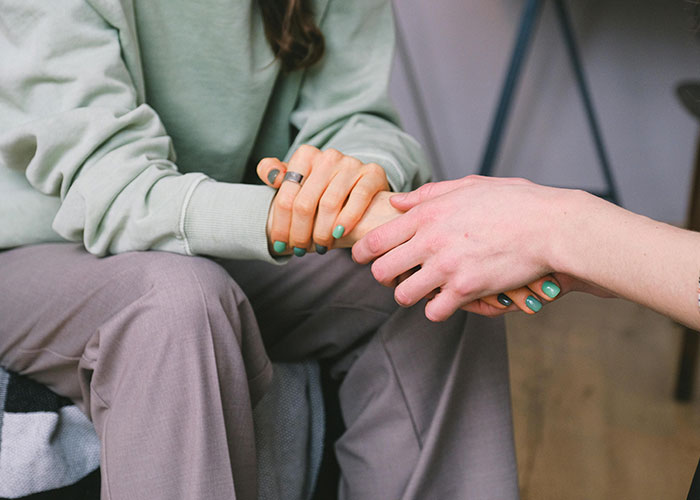 Two friends holding hands in a comforting gesture, representing complex feelings about dating the same guy.