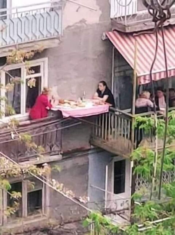 Three people sharing a meal on a narrow balcony, a wholesome moment providing comfort amid current world horrors.