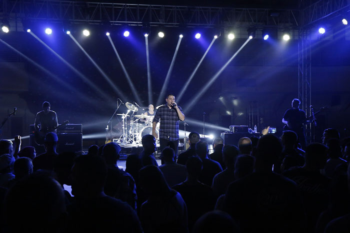 Band performing at a concert with lead singer and audience under bright stage lighting and spotlights.