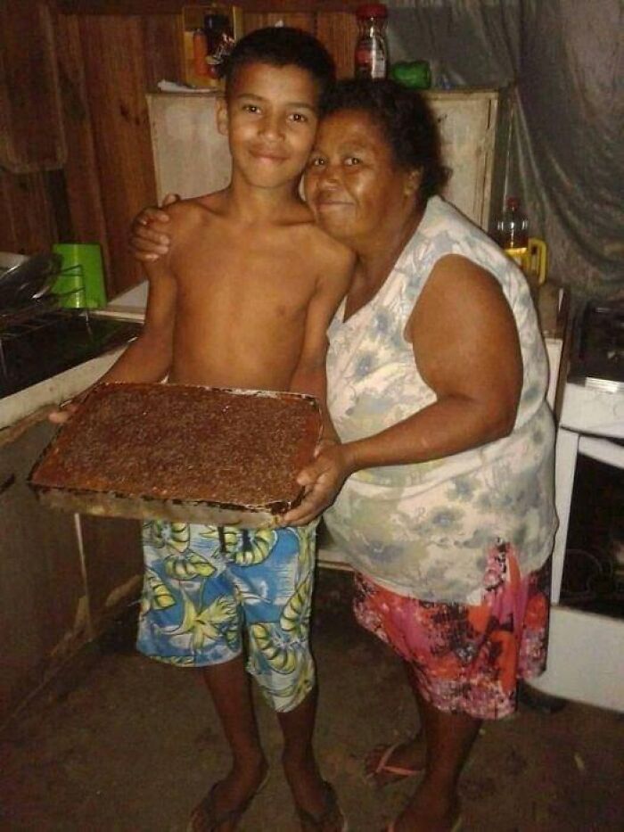 Boy and woman smiling together in a kitchen, holding a homemade baked dessert in a wholesome moment.