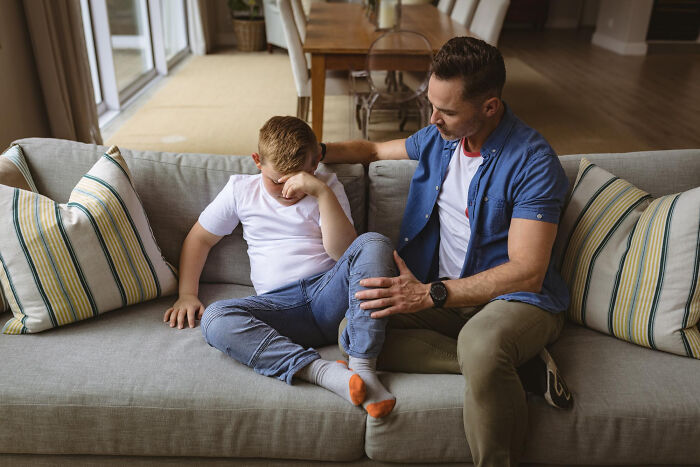Father comforting upset son on sofa, sharing life-changing sentences that have been tattooed on their hearts.
