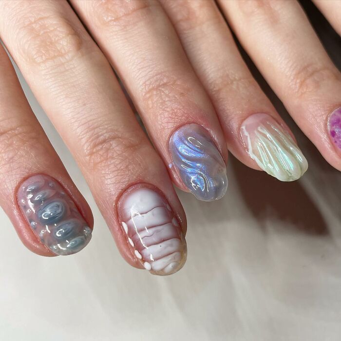 Close-up of unconventional nail designs with textured and iridescent effects showcasing creative nail art techniques.