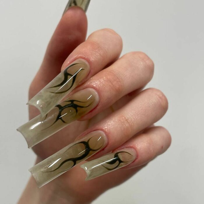 Long clear nails with black flame designs on natural-colored nail beds in a creative and bold nail design style.