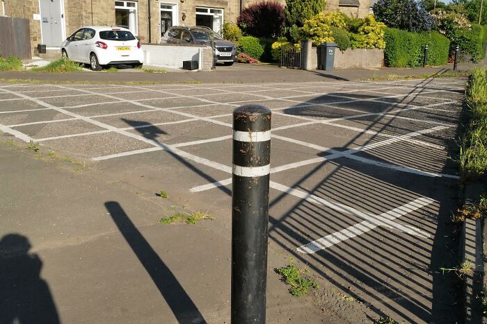 Black bollard casting a shadow that humorously aligns with the street photo capturing the funny side of life outdoors.