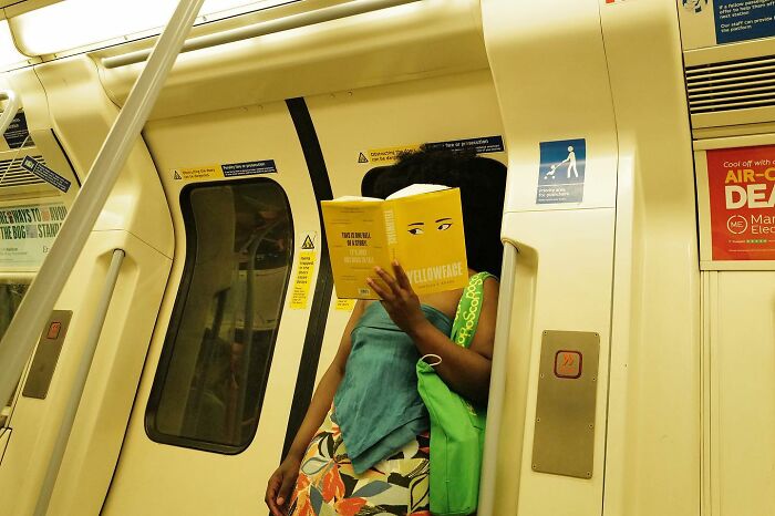Woman reading a book on a subway train, a funny street photo capturing the humorous side of life.