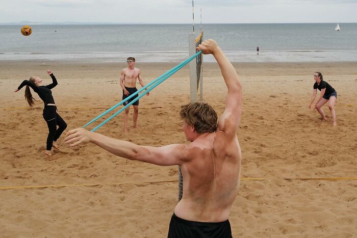 Young man using a giant slingshot on a beach volleyball court in a brilliant street photo capturing the funny side of life.