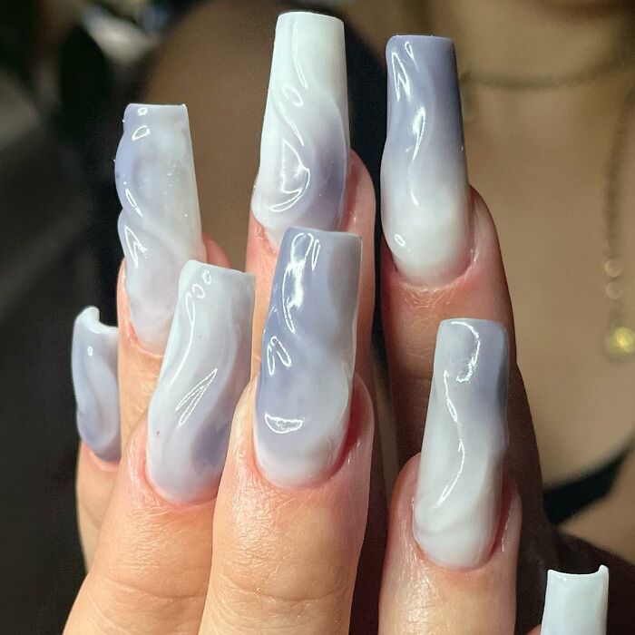 Long coffin-shaped nails with glossy marble nail designs in soft lavender and white shades.