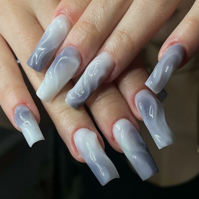 Long coffin-shaped nails with glossy marble nail designs in soft lavender and white shades.