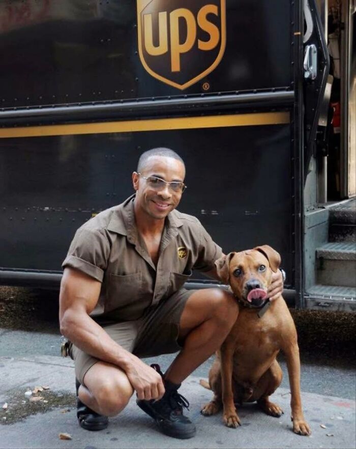 UPS driver kneeling and smiling beside an adorable dog during a delivery with UPS truck visible in background