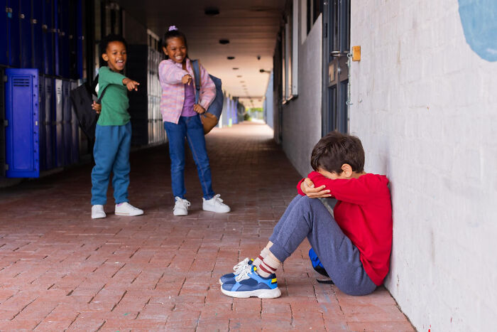 Two children laughing and pointing at a boy sitting alone, illustrating mind-boggling conversations adults had with kids.