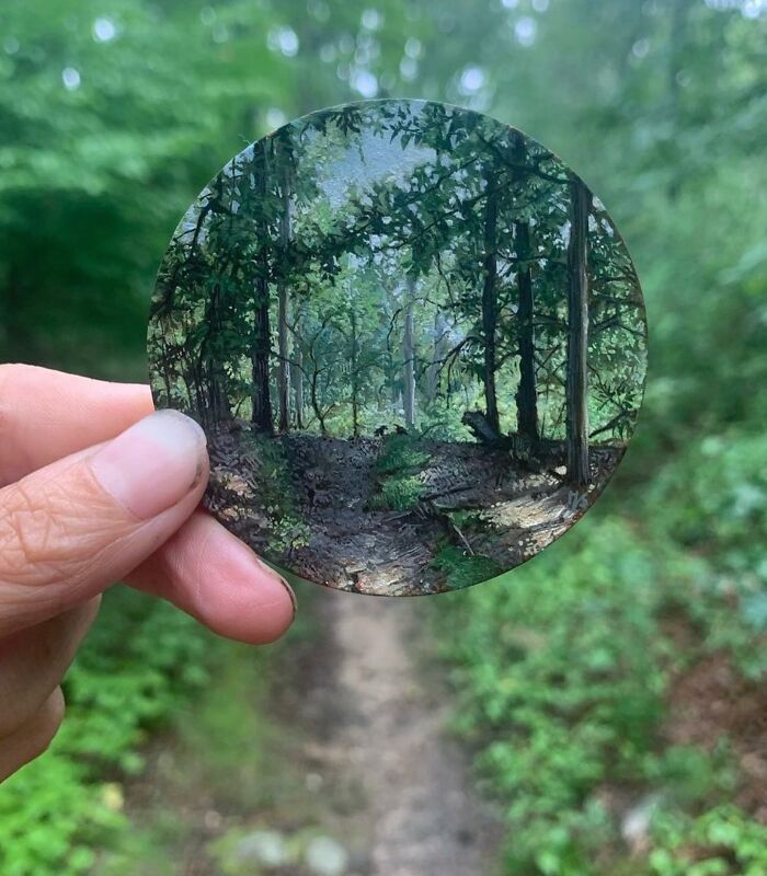 Hand holding a small detailed painting of a forest scene that shows the beauty of the natural world.